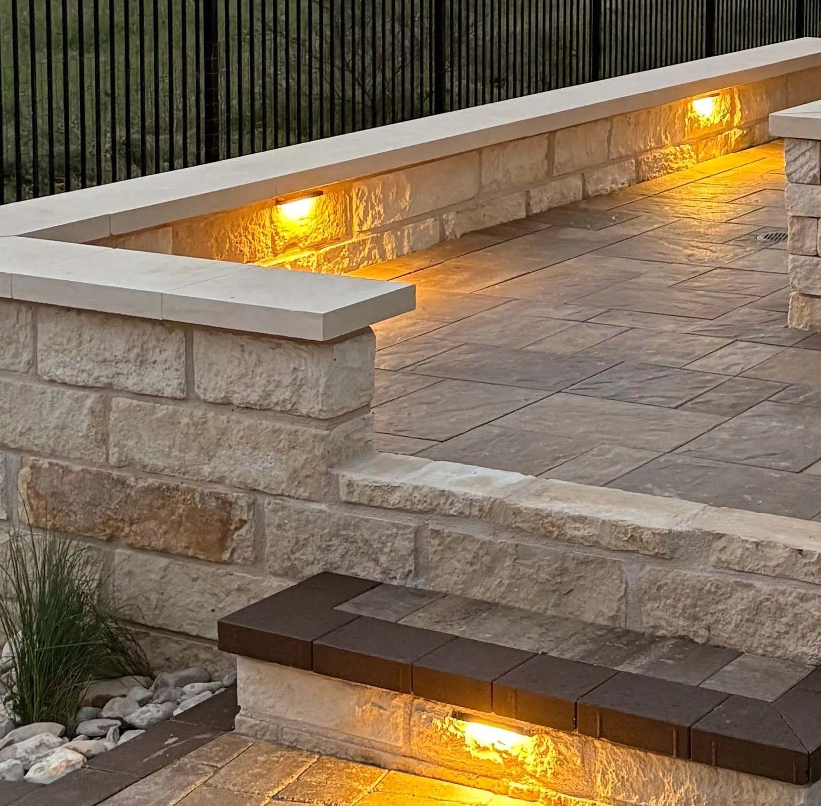 Close view of a cut-limestone seat wall with a light under its cap, a river-rock bed and a lit step beside it