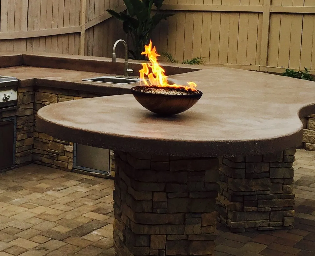 Copper fire bowl burning on a curved concrete bar top supported by stacked-stone columns